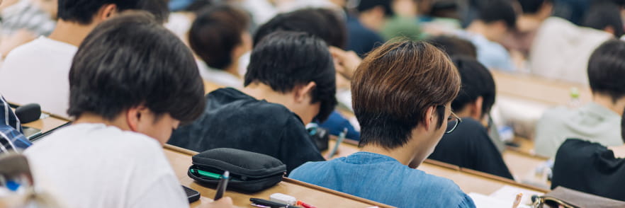 大学の講義室で多くの学生がノートを取りながら授業を受けている様子