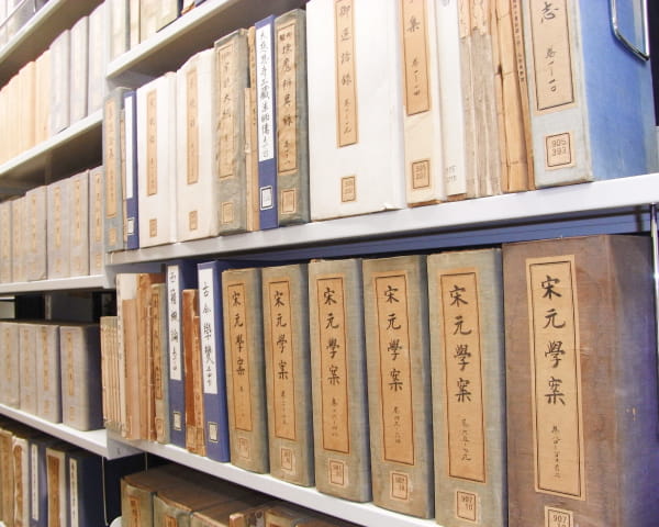 書棚にずらりと並んだ和綴じや漢籍風の古書が保管された図書館や研究施設の一角