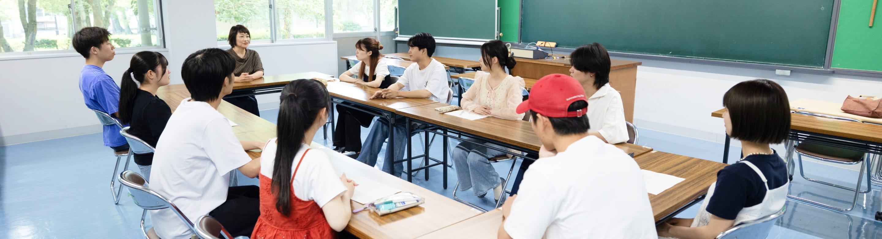 教室内で学生たちが机を囲み、教員と向き合って議論や発表を行っている様子