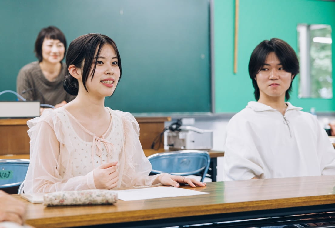 教室で女子学生が前向きに発言している様子で、隣に男子学生が座っている