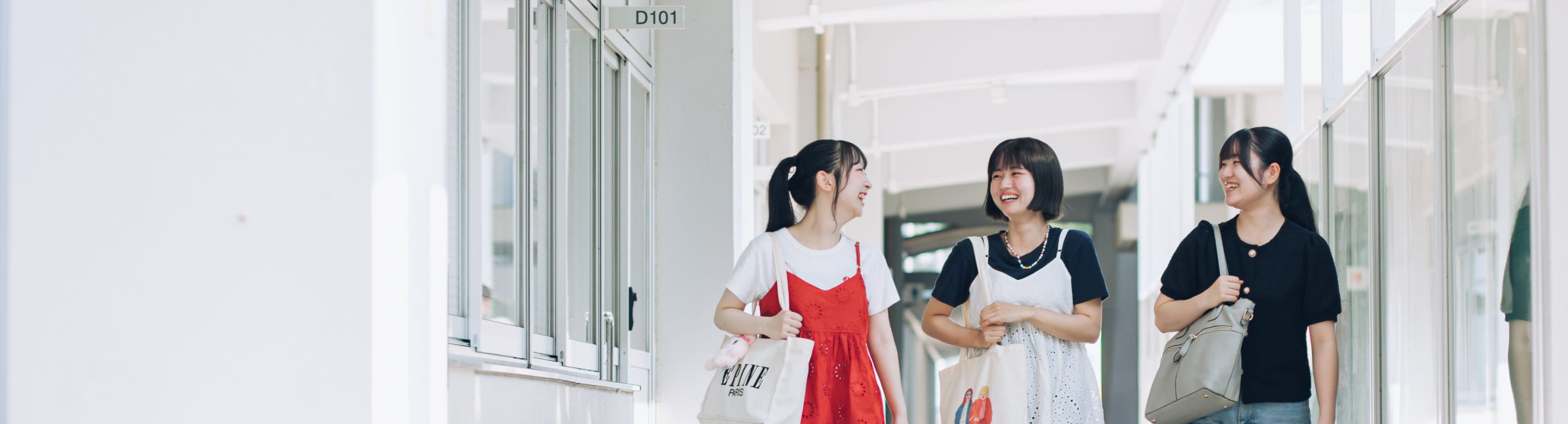 校舎の廊下を歩きながら笑顔で会話する3人の女子学生の様子