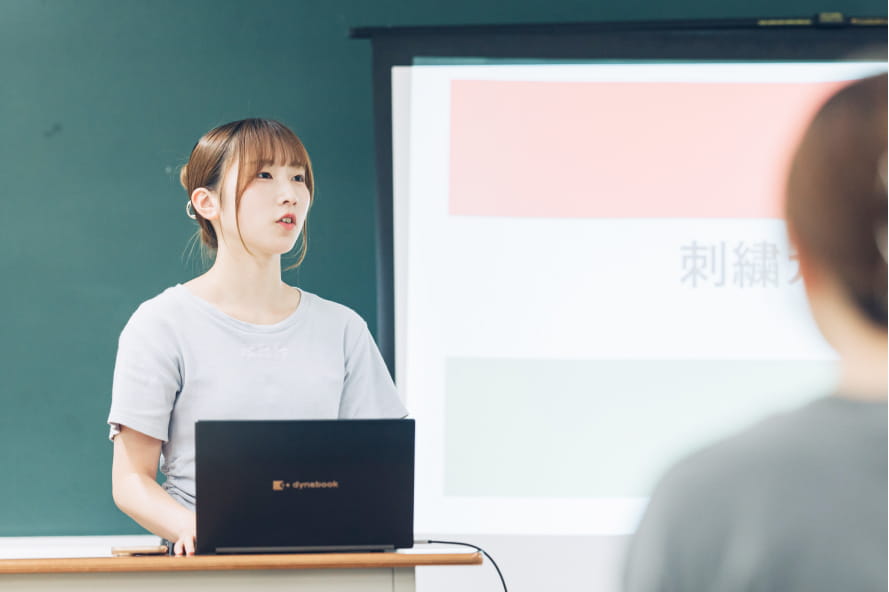 教室でノートパソコンを使いながらプレゼンテーションを行っている女子学生の様子
