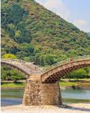 アーチ型の木造橋が川を渡っており、背景には緑豊かな山が広がっている風景