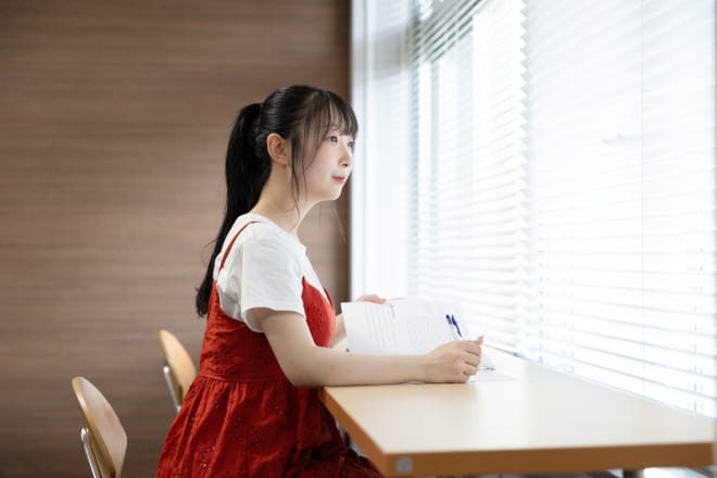 窓際のカウンター席でノートを開きながら外を見つめる女性の様子