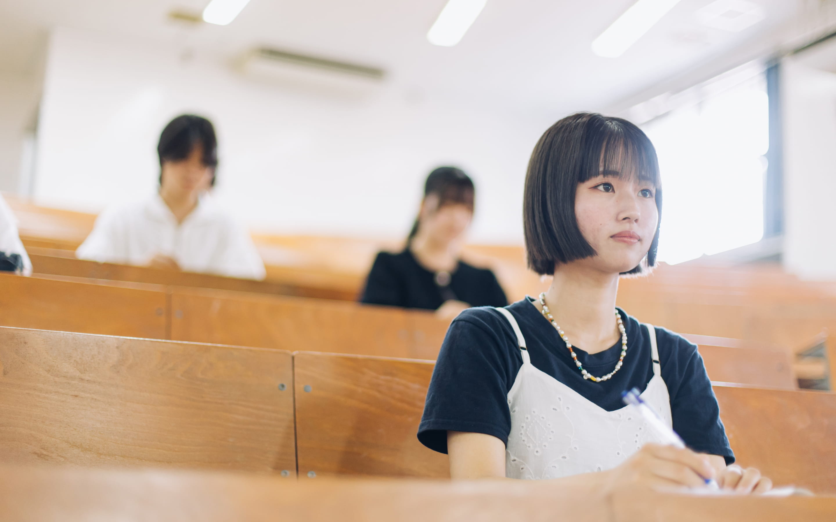 大学の講義室でノートを取りながら講義を受けている女子学生の様子