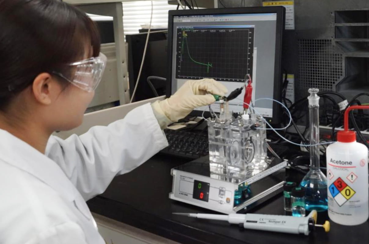 白衣と保護メガネを着用した学生が、実験装置を操作している研究室内の様子