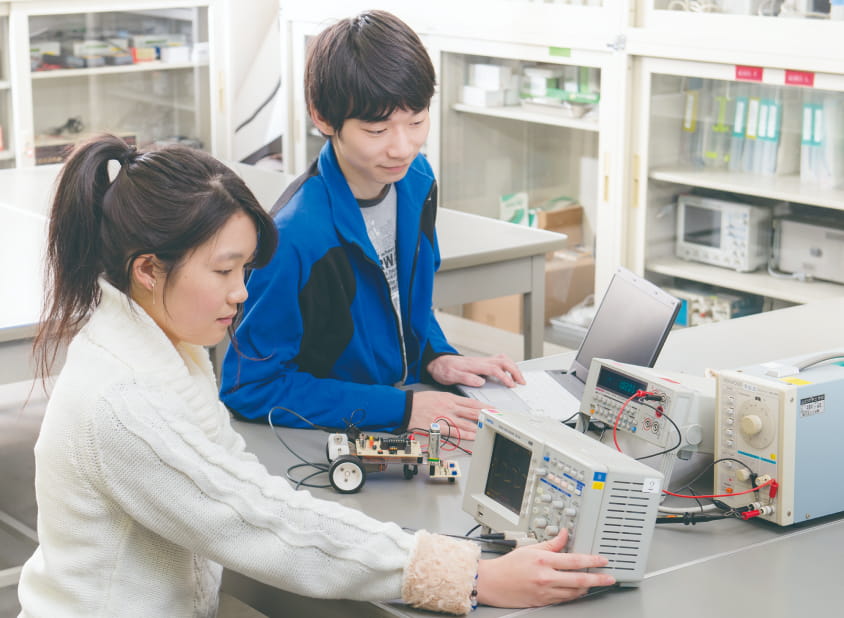 実験室内で学生が電子計測機器を操作し、回路の動作を確認している様子
