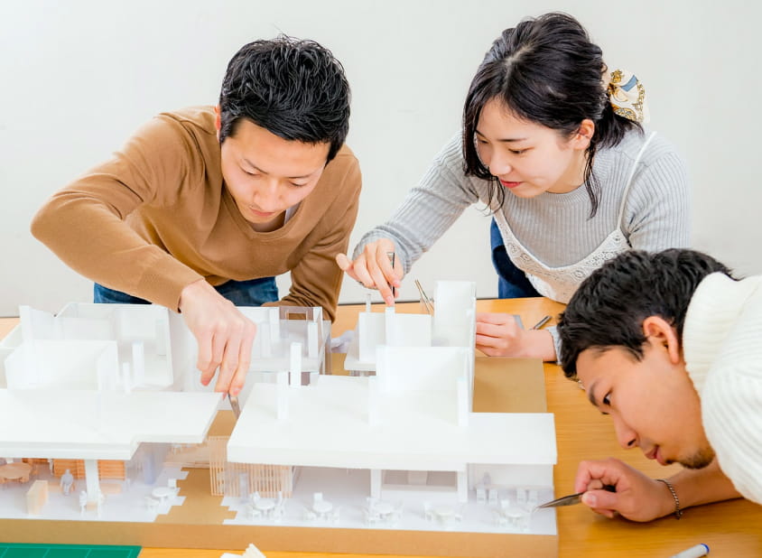 建築模型を囲んで学生たちがピンセットを使い、細部を丁寧に作業している様子
